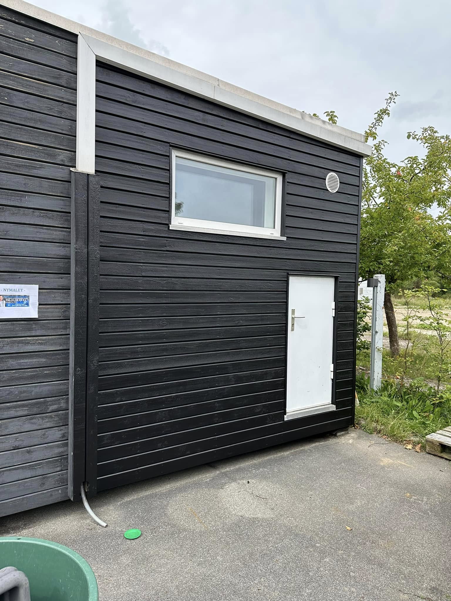 Sortmalet træfacade med hvid dør og vindue